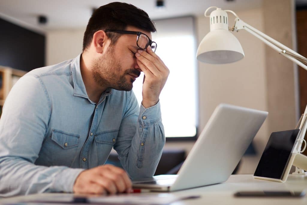 Young man has a headache at work while working on a laptop and dealing with stress